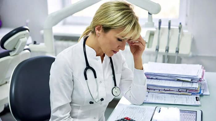 Woman in scrubs surrounded by paperwork illustrating challenges for Colorado Springs service businesses.